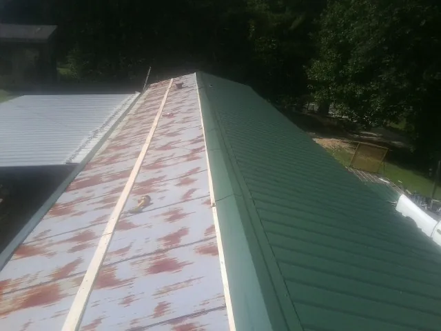 Old rusted panels beside newly installed green metal roofing — Wind Damage Roof Repair by Roofing Brothers in Cold Spring