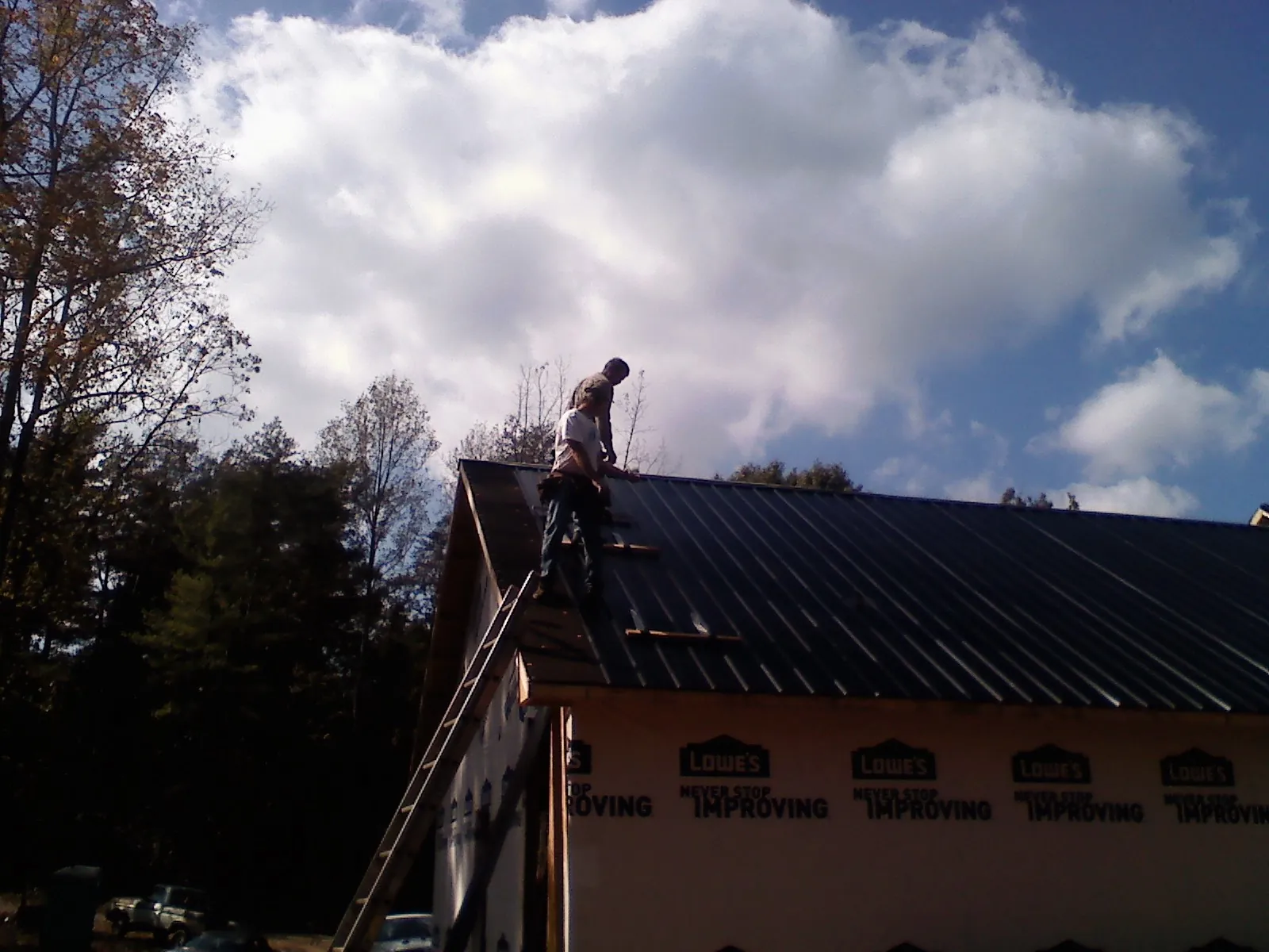 Roofer fastening dark metal panels high against a cloudy sky, from a Roof Inspection job in Cold Spring
