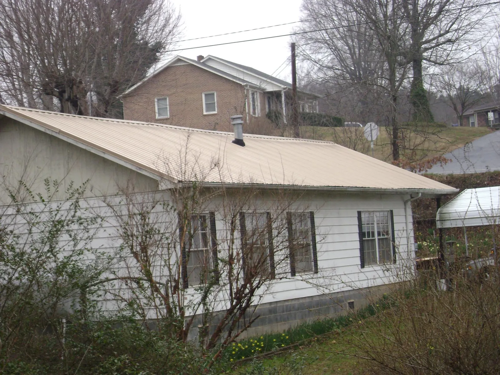 Tan metal roof on a white sided house set into a hillside — Commercial Roofing by Roofing Brothers in Cold Spring